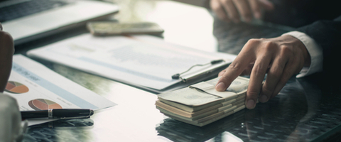 man offers pile of money across table